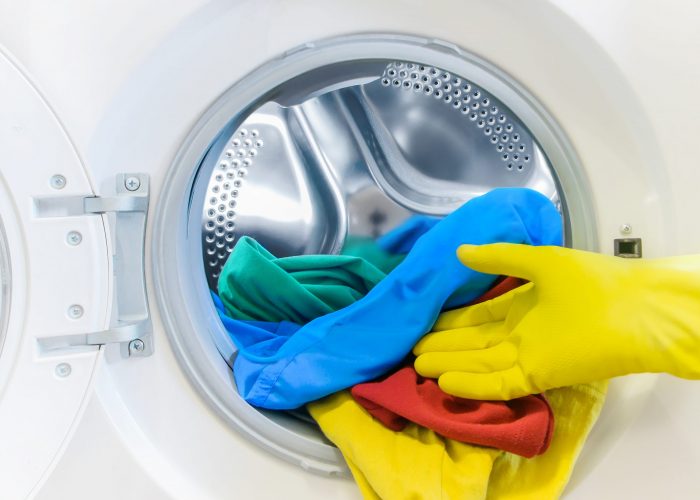 Hand in a yellow glove takes the color Laundry out of the washing machine