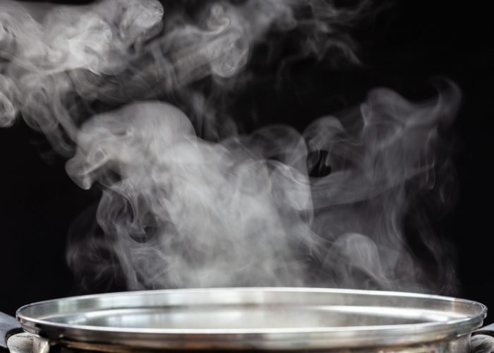 Traditional silver cooking pot with white smoke while cooking on black background