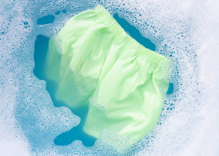 Green baby shorts soak in baby laundry detergent water dissolution, washing cloth, blue background, Laundry concept.